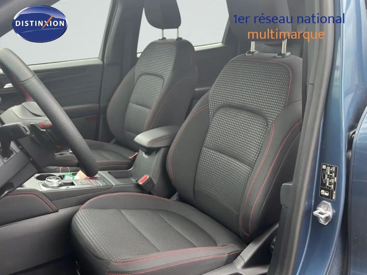 Vue intérieure côté conducteur du Ford Kuga 2024 bleu chrome, sièges tissu noir avec surpiqûres rouges et volant multifonction.