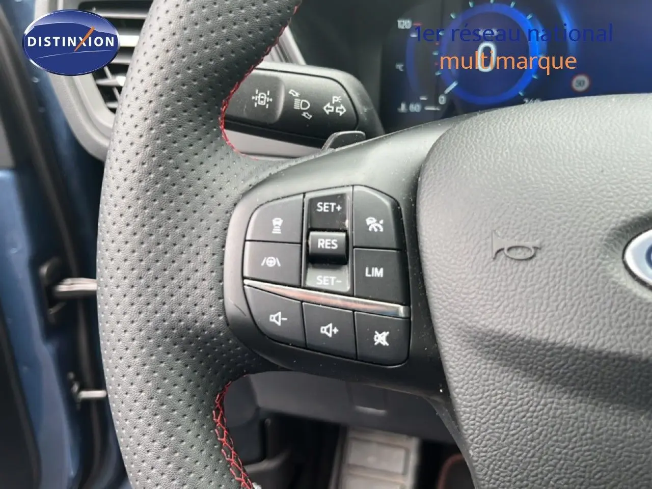 Gros plan sur le volant perforé avec surpiqûres rouges du Ford Kuga bleu chrome, montrant les commandes multifonctions à gauche.