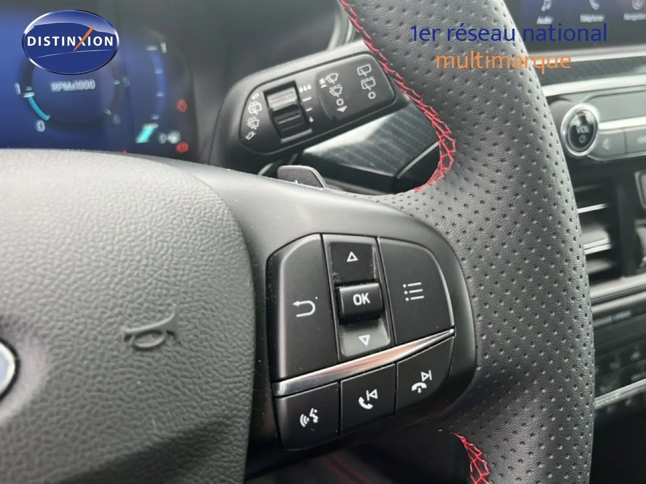 Gros plan sur le volant perforé avec surpiqûres rouges du Ford Kuga 2024, montrant les commandes multifonctions.