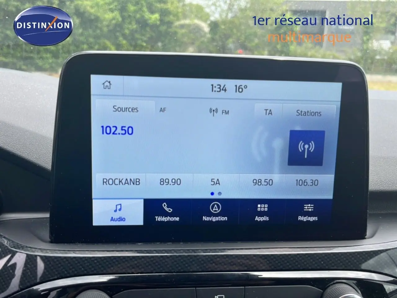 Écran tactile central du Ford Kuga 2024 affichant la radio FM, avec tableau de bord en finition noire.