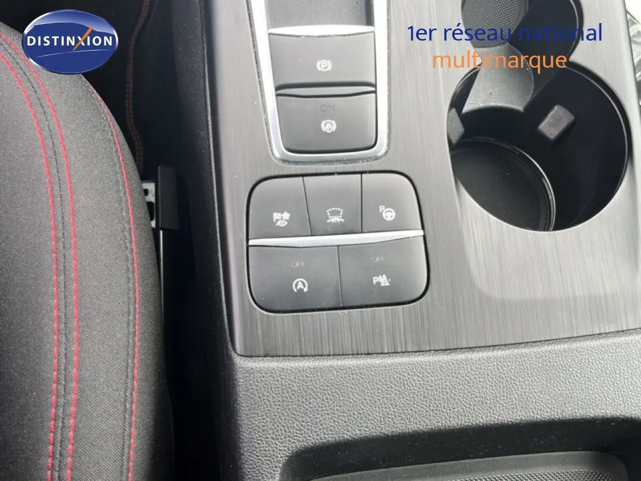 Gros plan sur la console centrale du Ford Kuga 2024 bleu chrome, avec boutons de contrôle et porte-gobelet visible.