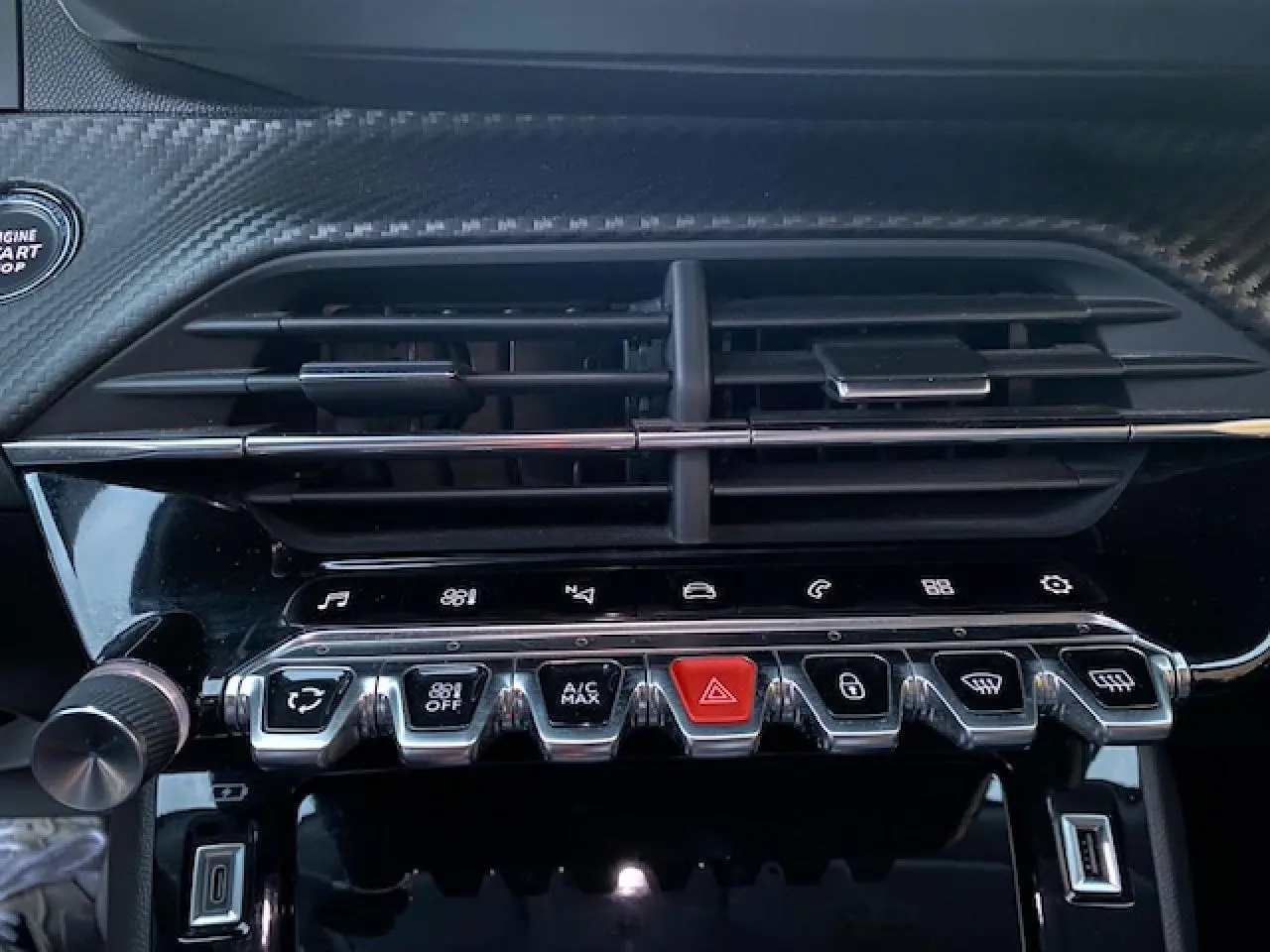 Gros plan sur la console centrale noire brillante du Peugeot 2008 avec commandes climatisation et bouton rouge d'alerte