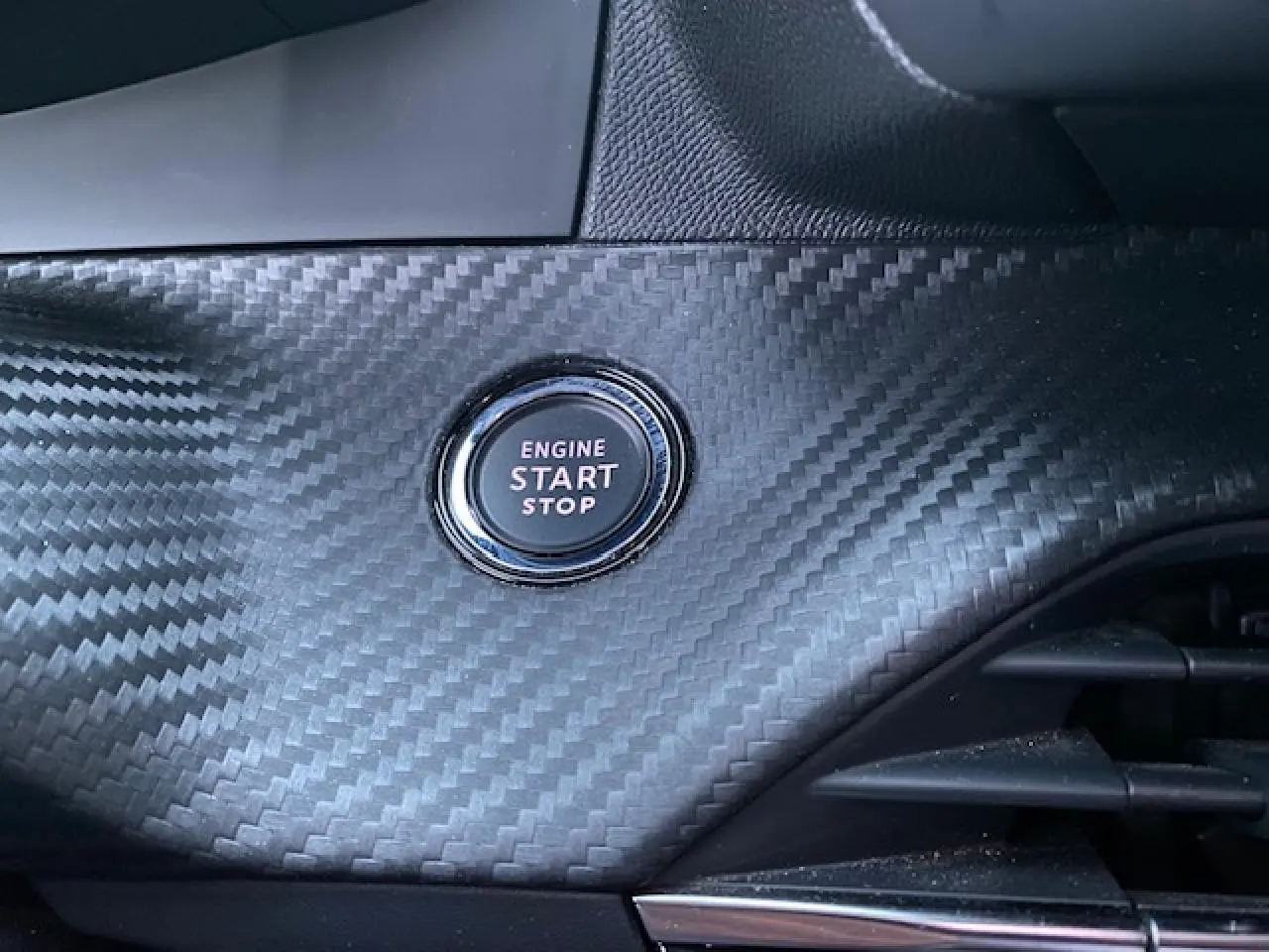 Bouton démarrage moteur "Engine Start Stop" sur tableau de bord en carbone du Peugeot 2008 blanc, vue intérieure rapprochée.