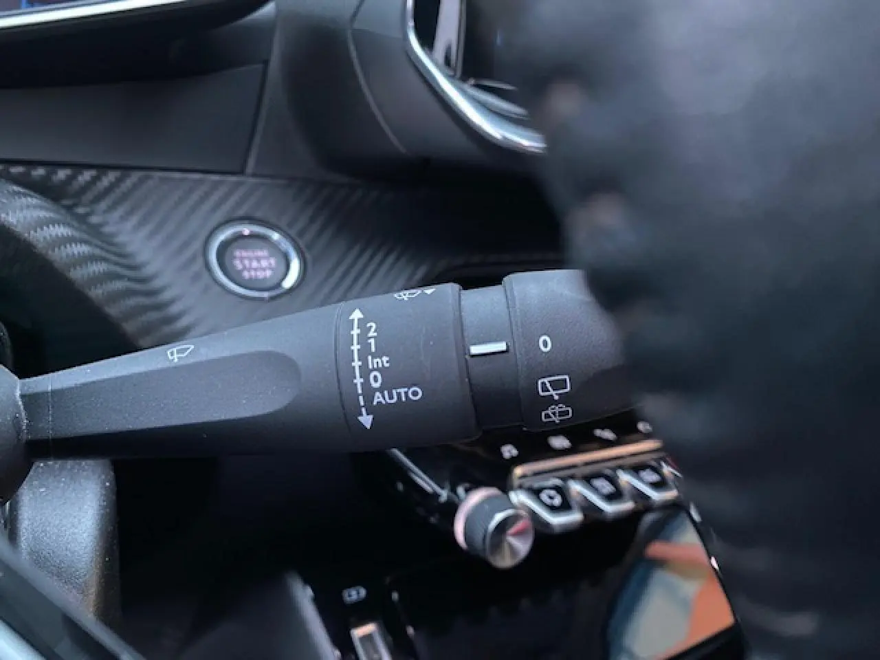 Gros plan sur la commande d'essuie-glace à gauche du volant dans l'habitacle noir d'une Peugeot 2008 blanche de 2020.