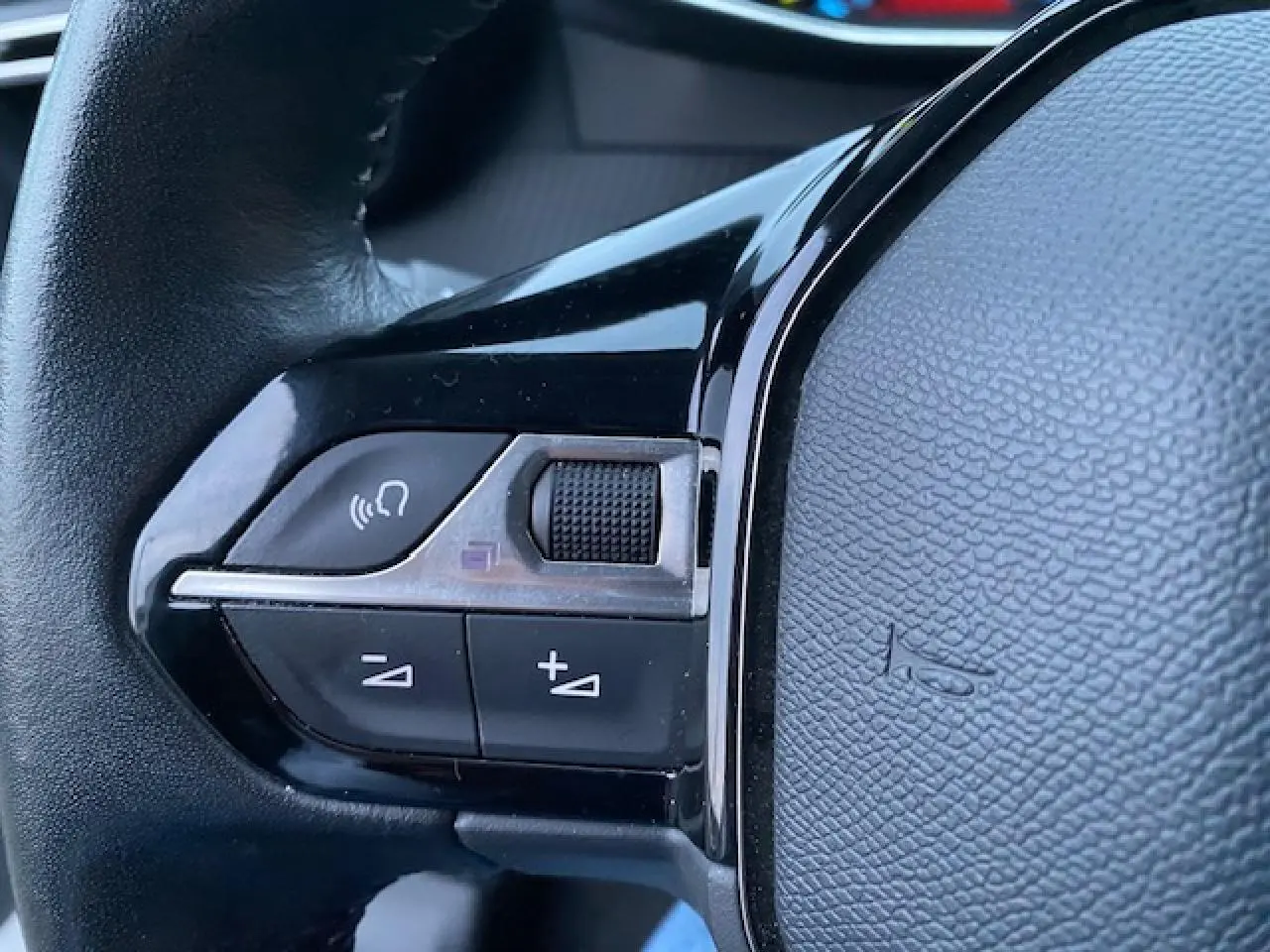 Gros plan sur les commandes vocales et volume au volant noir du Peugeot 2008 blanc de 2020.