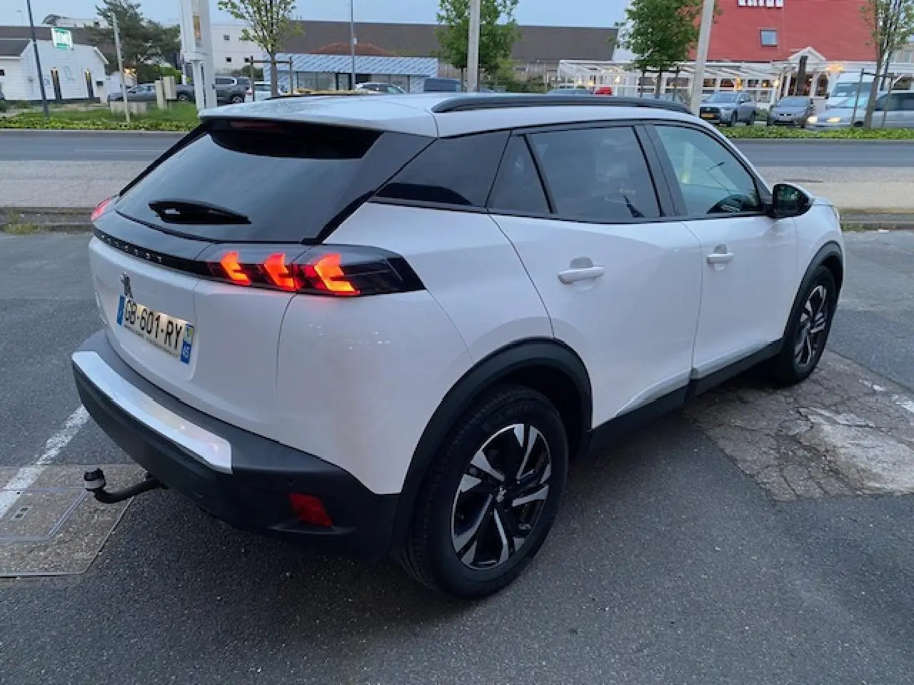 Peugeot 2008 blanc vue 3/4 arrière droit avec jantes bi-tons et attelage col de cygne visible.