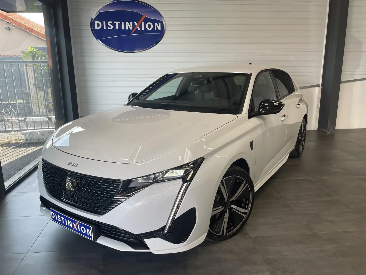 Peugeot 308 GT blanche vue en 3/4 avant droit, avec calandre noire vernie et jantes alliage 18 pouces.