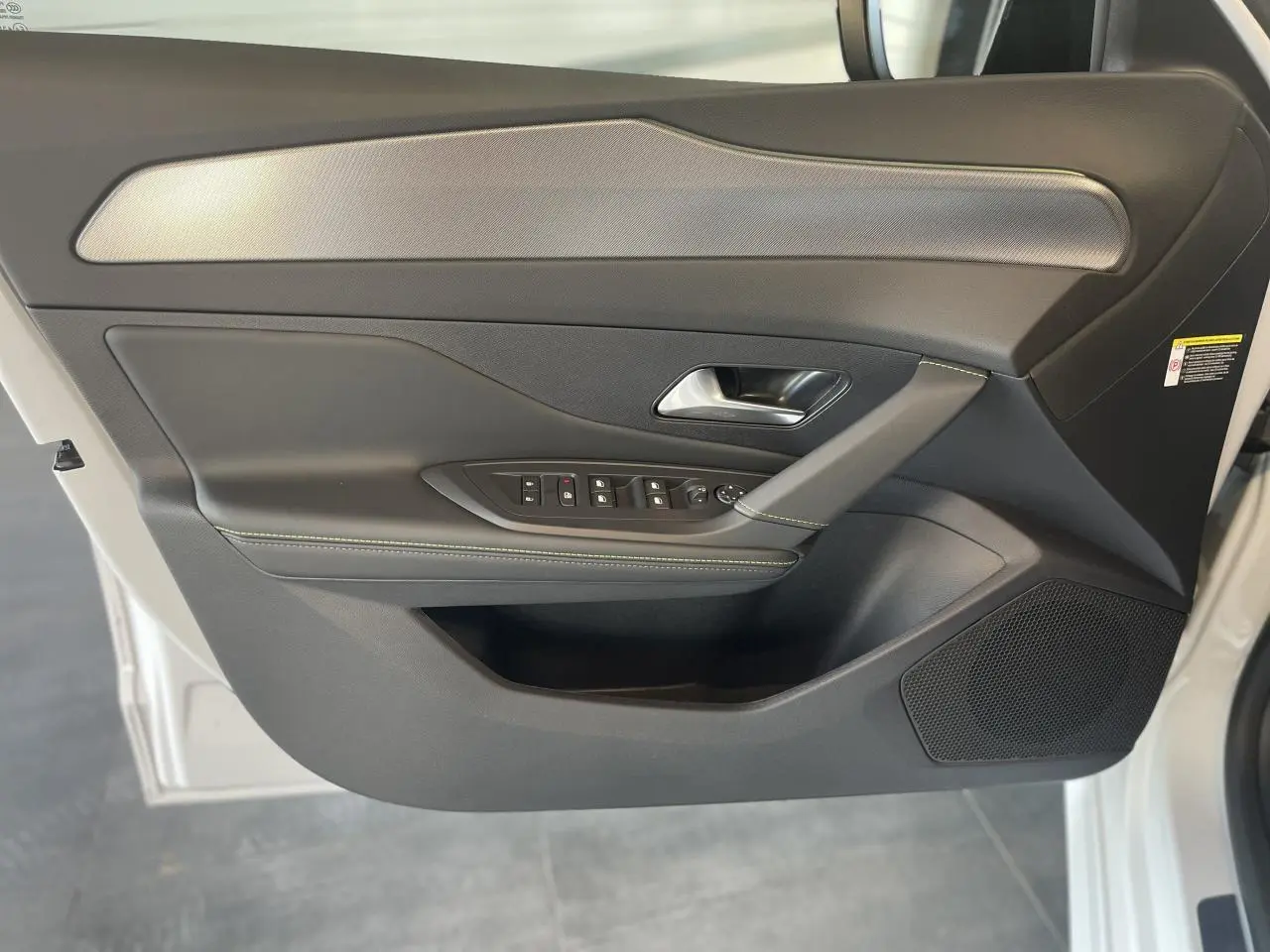 Porte avant gauche ouverte d'une Peugeot 308 blanche 2025, garniture noire avec surpiqûres vertes et insert aluminium.