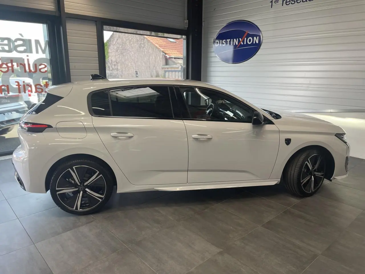 Peugeot 308 blanche vue de profil côté gauche en intérieur avec jantes alliage noires et vitres teintées.