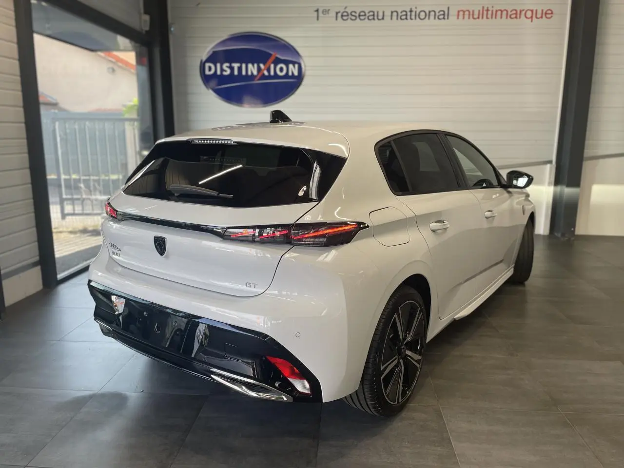 Vue 3/4 arrière droite d'une Peugeot 308 GT blanche avec feux arrière LED et jantes alliage 18 pouces en showroom.