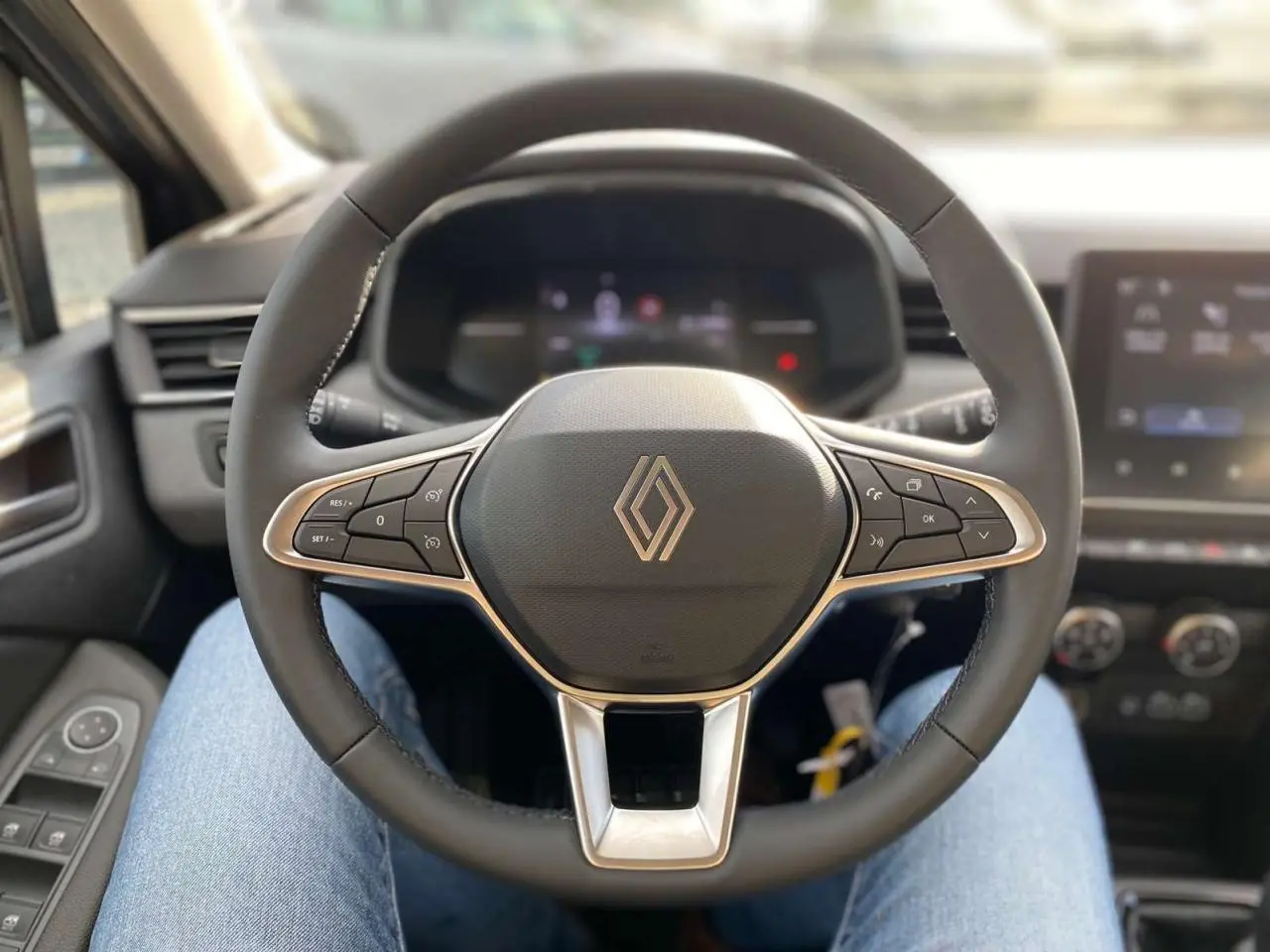 Vue centrée sur le volant noir de la Renault Clio 2025 avec commandes intégrées et tableau de bord flou en arrière-plan.