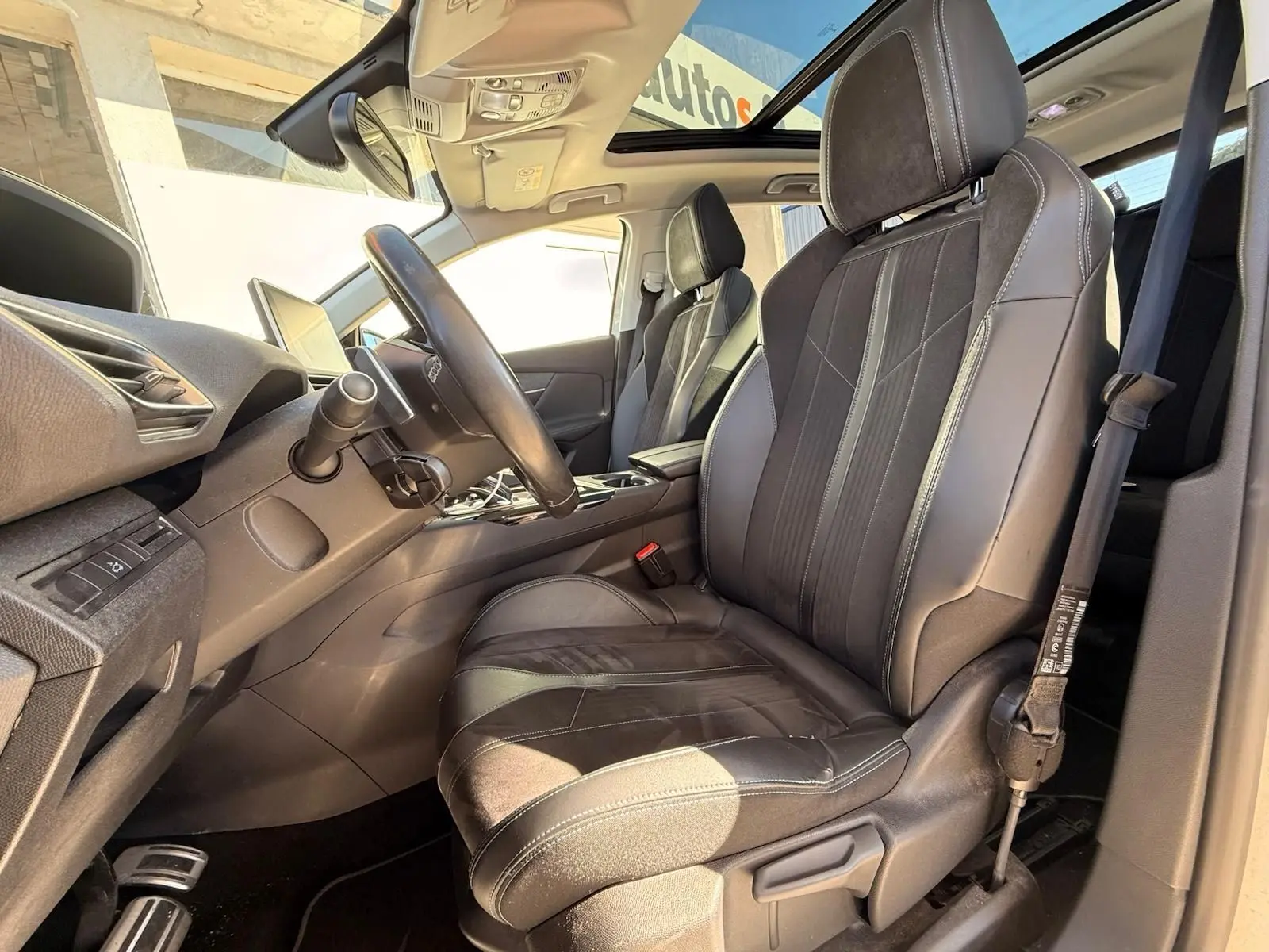 Intérieur du Peugeot 3008 2019, vue côté conducteur, sièges en cuir noir avec surpiqûres blanches et toit ouvrant panoramique.