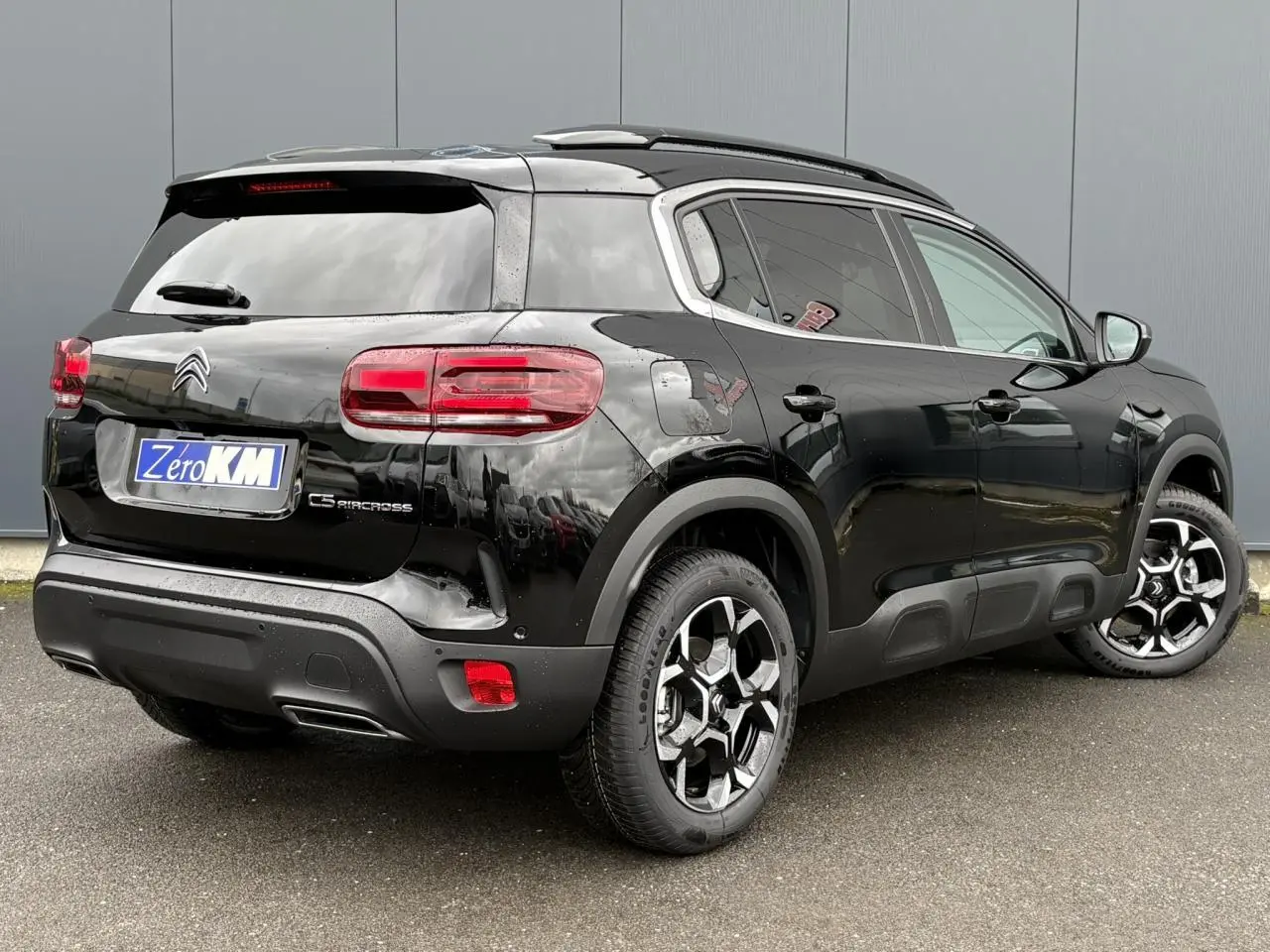 Vue 3/4 arrière droite d'un Citroën C5 Aircross Hybrid noir Perla avec jantes alliage bi-ton et barres de toit noires.