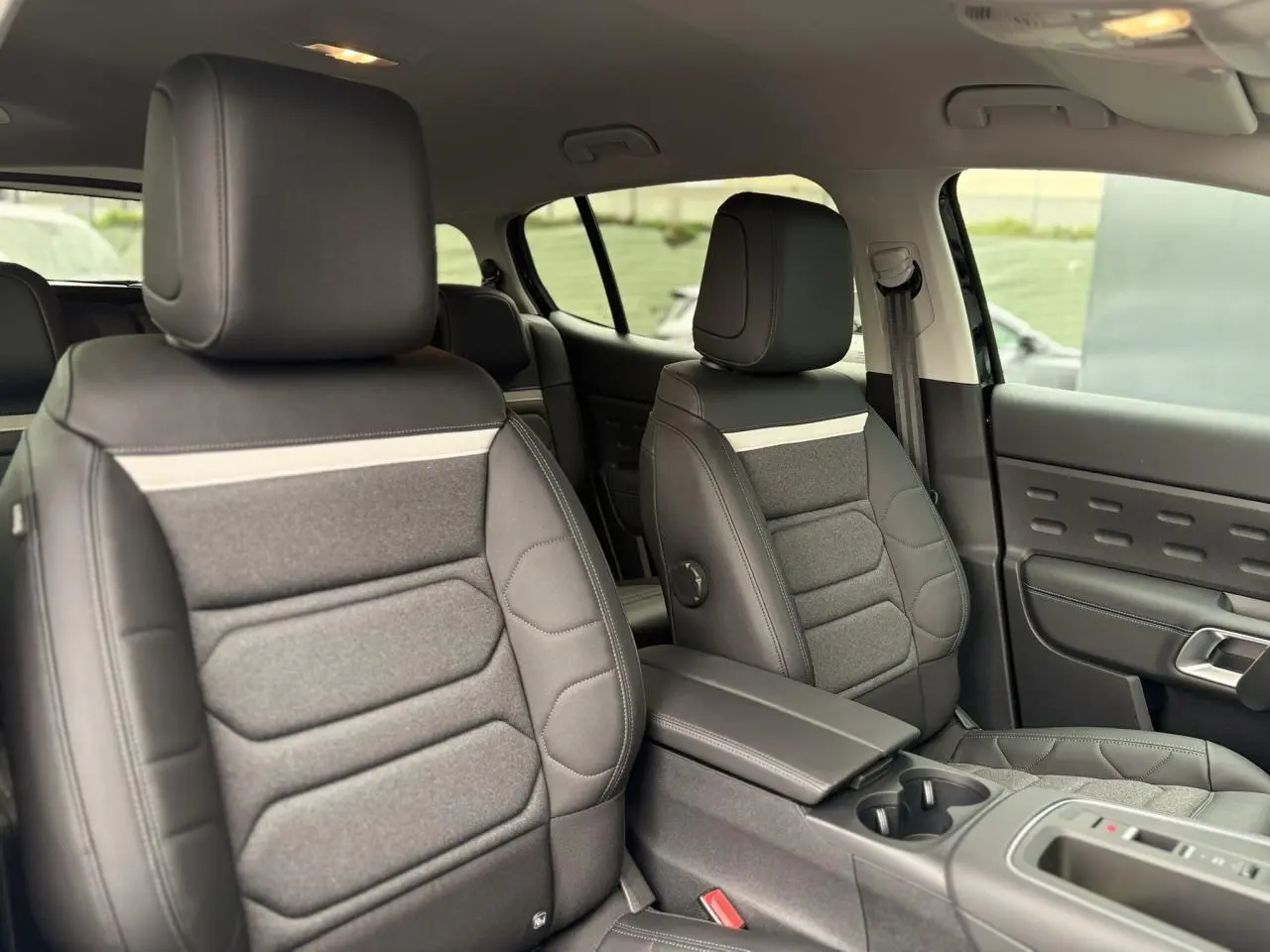 Vue intérieure côté droit des sièges avant en tissu et cuir noir avec accoudoir central du Citroën C5 Aircross Hybrid 2025.
