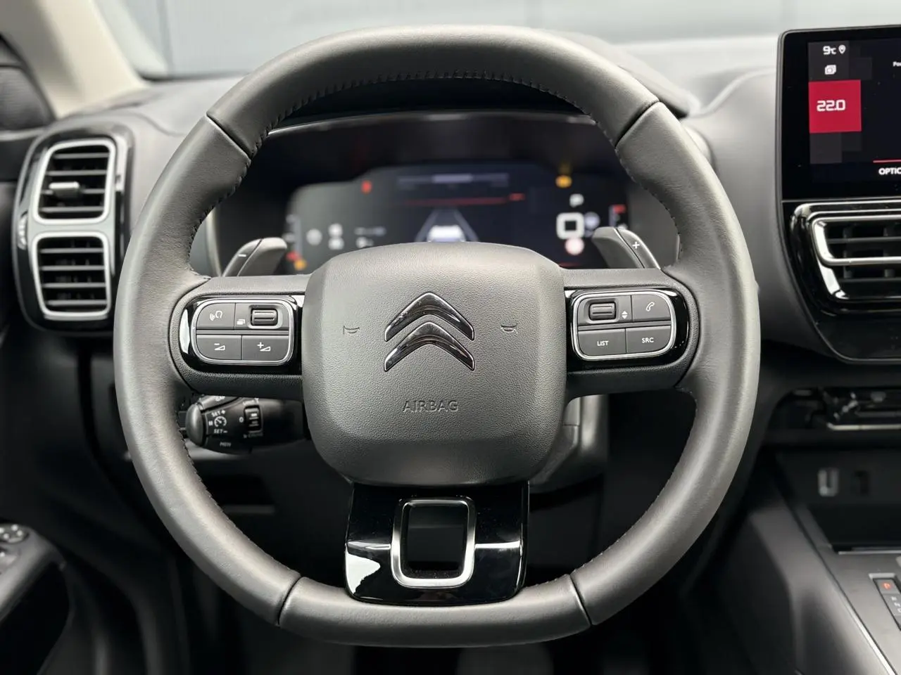 Vue rapprochée du volant cuir noir avec commandes intégrées du Citroën C5 Aircross Hybrid 2025, tableau de bord et écran tactile visibles.