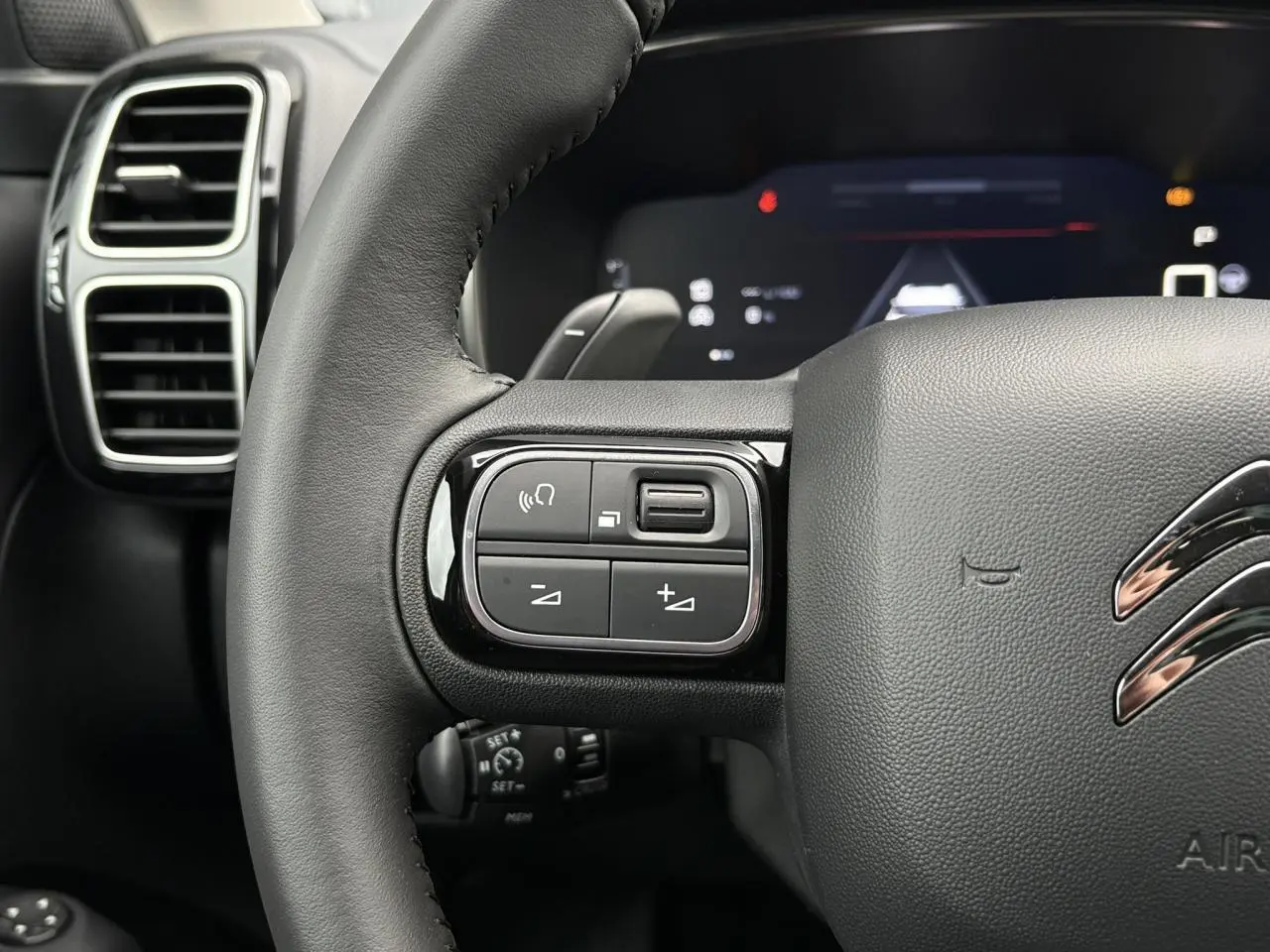 Gros plan sur le volant noir cuir de la Citroën C5 Aircross Hybrid 2025, avec commandes intégrées et logo chromé.