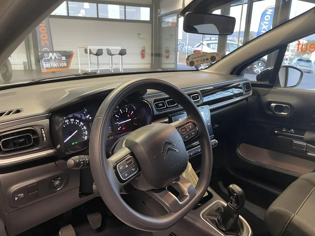 Vue intérieure côté conducteur du tableau de bord et volant noir de la Citroën C3 beige clair 2024 avec boîte manuelle.