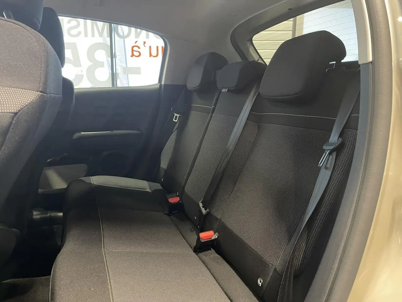 Vue intérieure côté droit montrant la banquette arrière noire avec ceintures de sécurité sur Citroën C3 beige clair 2024.