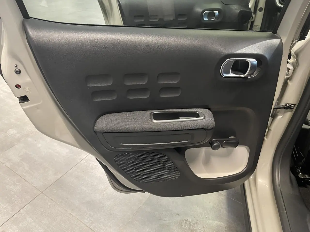 Vue intérieure côté gauche de la porte arrière beige clair d'une Citroën C3 2024 avec poignée chromée et manivelle de vitre.