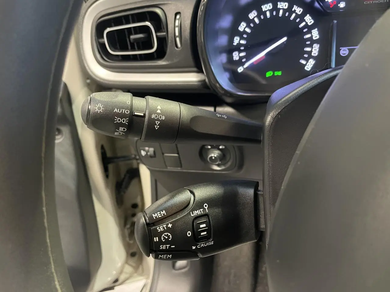 Gros plan sur les commandes au volant et le compteur digital d'une Citroën C3 beige clair 2024, intérieur noir.