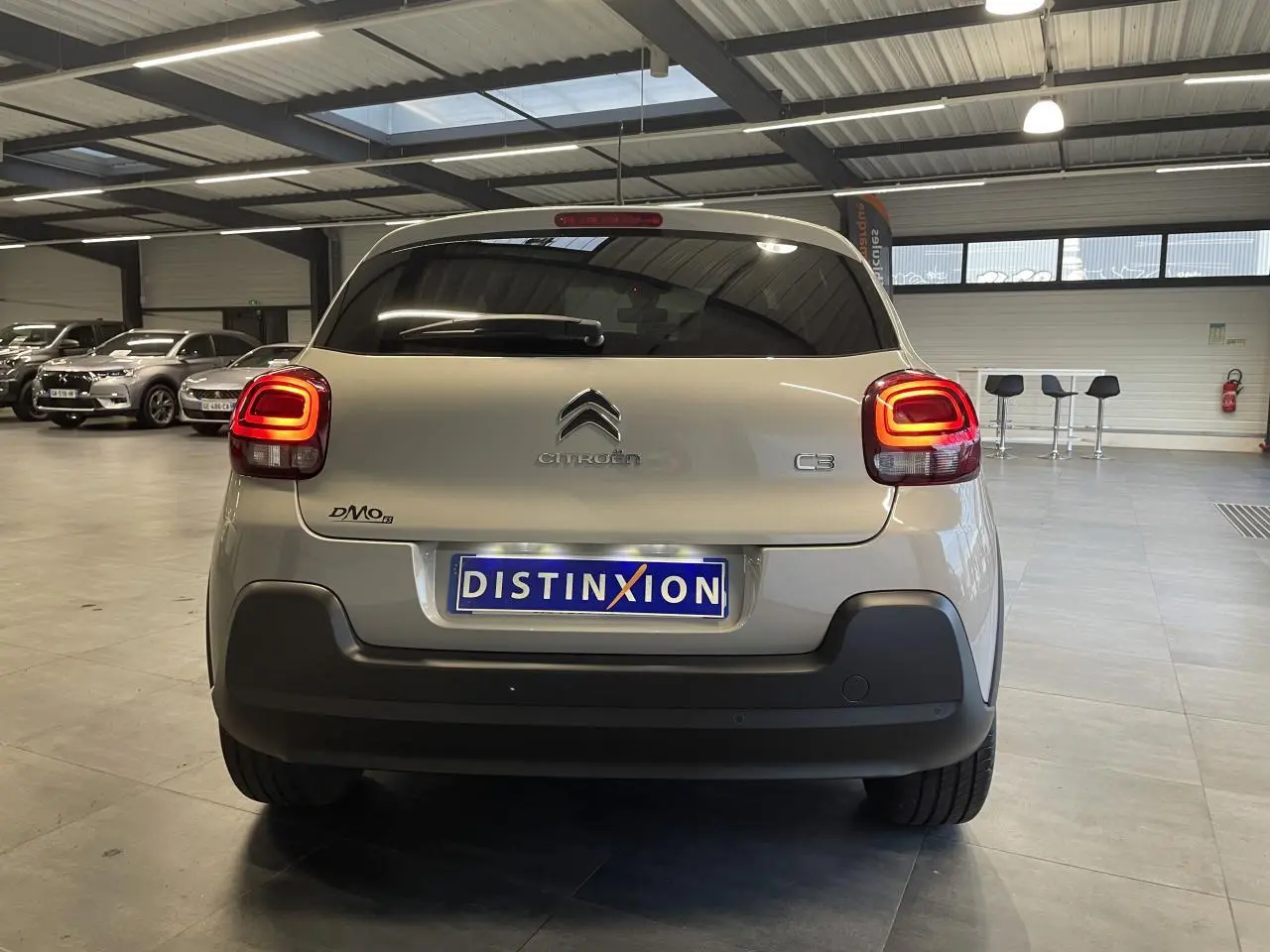 Vue arrière d'une Citroën C3 beige clair 2024 avec feux arrière à effet 3D et pare-chocs noir mat en intérieur showroom.