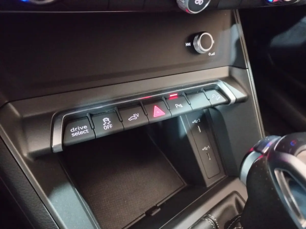 Gros plan sur la console centrale noire de l'Audi Q3 45 TFSI e 2021, montrant les boutons de contrôle et ports USB.