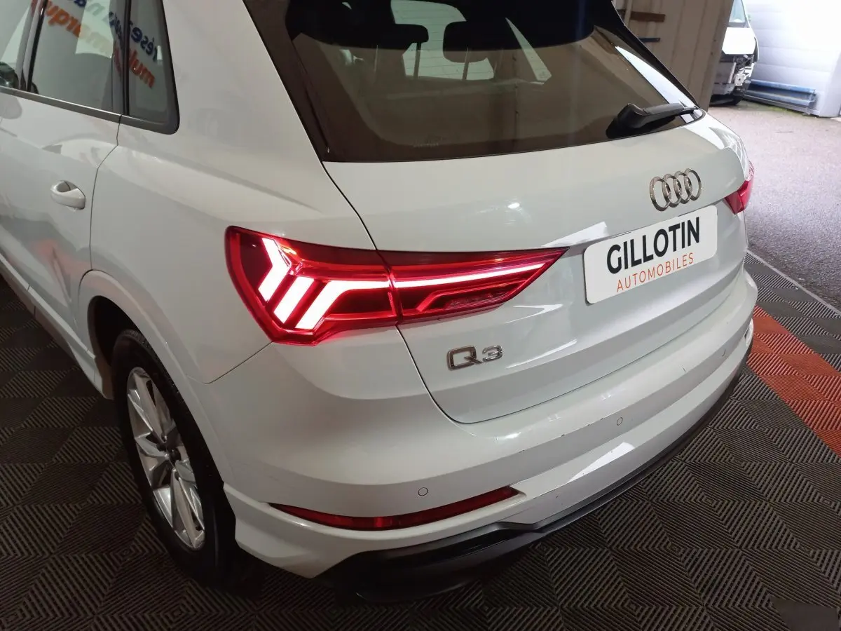 Vue 3/4 arrière droite d’un Audi Q3 blanc avec feux arrière LED allumés dans un showroom.