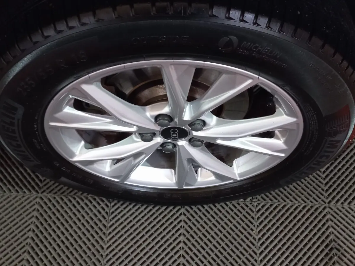 Gros plan sur la jante argentée en alliage de l'Audi Q3 blanc, avec pneu Michelin visible sur sol texturé.