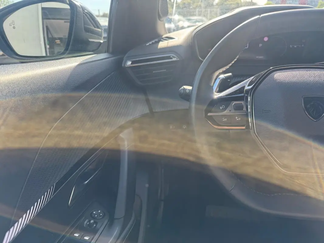 Vue intérieure côté gauche du Peugeot 2008 Hybrid 136 Allure 2025 noir, avec volant multifonction et commandes sur porte.