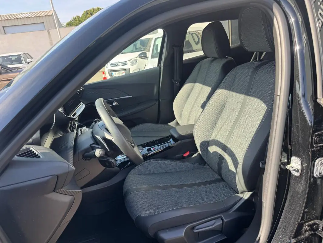 Vue intérieure côté conducteur du Peugeot 2008 Hybrid 136 Allure 2025 noir, montrant les sièges avant et le volant.