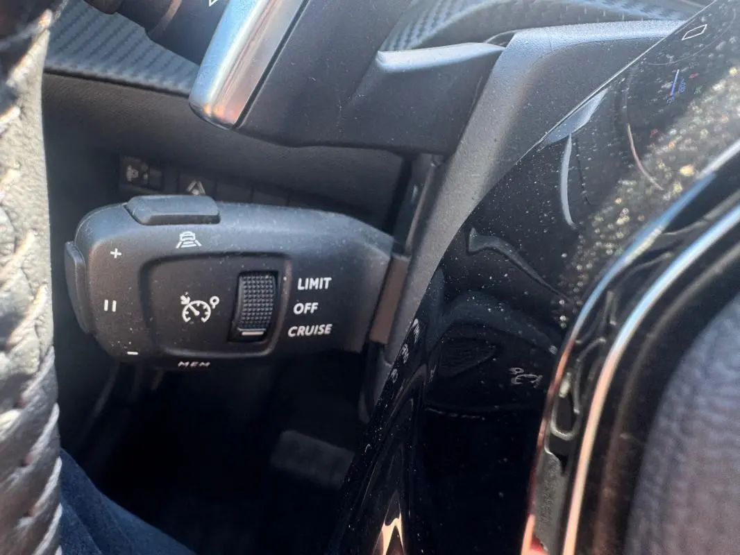 Gros plan sur la commande de régulateur de vitesse à gauche du volant dans l’habitacle noir du Peugeot 2008 Hybrid 136 Allure.