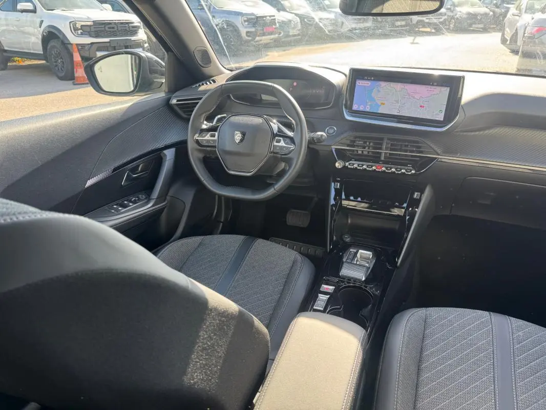 Intérieur du Peugeot 2008 Hybrid 136 Allure 2025, vue depuis l'arrière côté conducteur, avec écran tactile et volant compact noir.