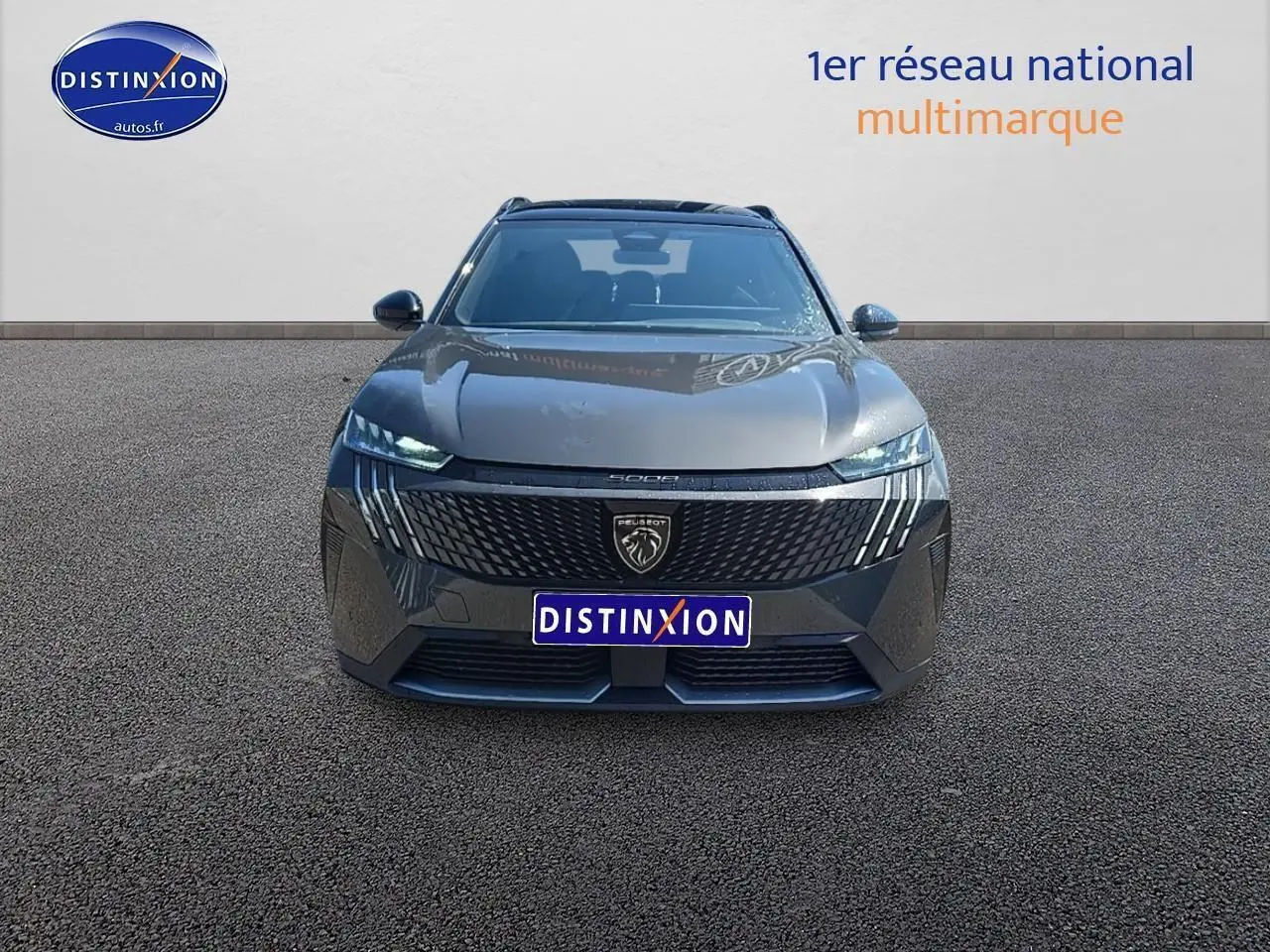 Vue frontale d'un Peugeot 5008 Hybrid 145 GT gris titane avec calandre noire et phares LED allumés.