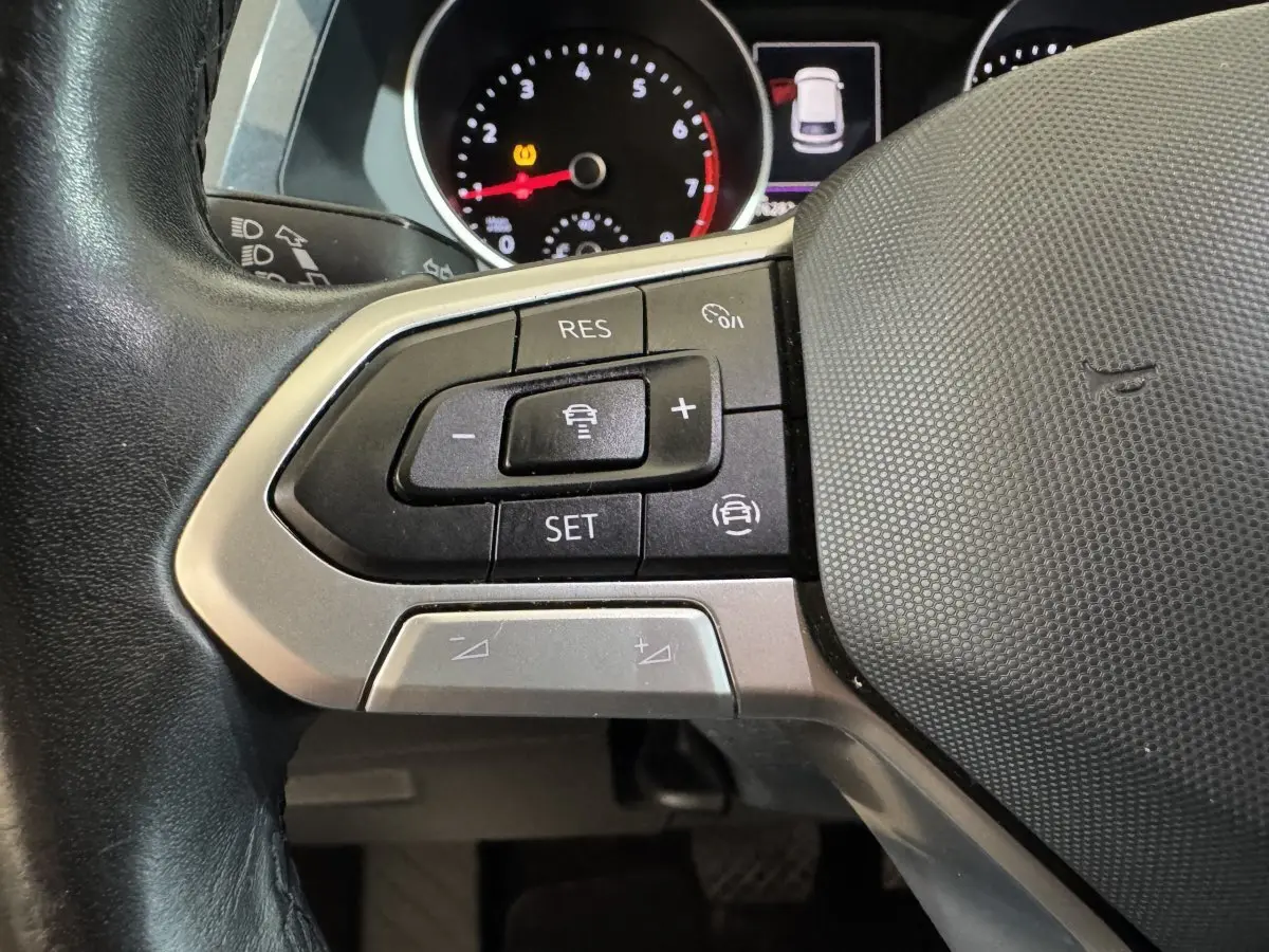 Gros plan sur les commandes multifonctions du volant cuir du Volkswagen Tiguan 1.5 TSI bleu, avec tableau de bord partiellement visible.