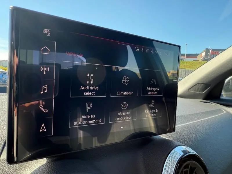 Écran tactile central de l'Audi Q2 35 TDI S line 2025 affichant les réglages de conduite et d'aide au stationnement.