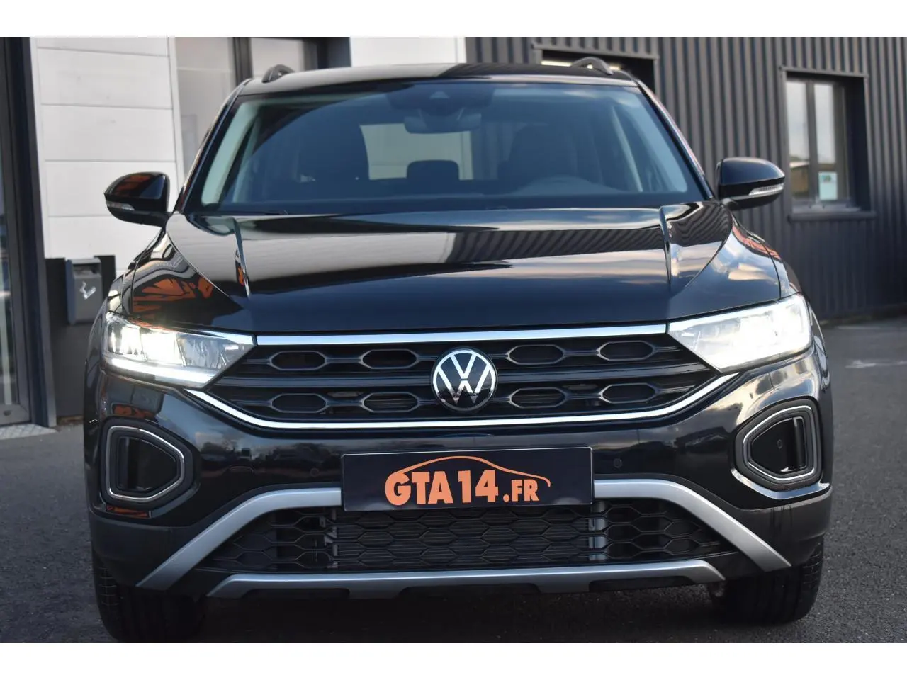 Vue frontale du Volkswagen T-Roc 2025 en noir Grenadilla Metallic avec calandre hexagonale et feux LED allumés.