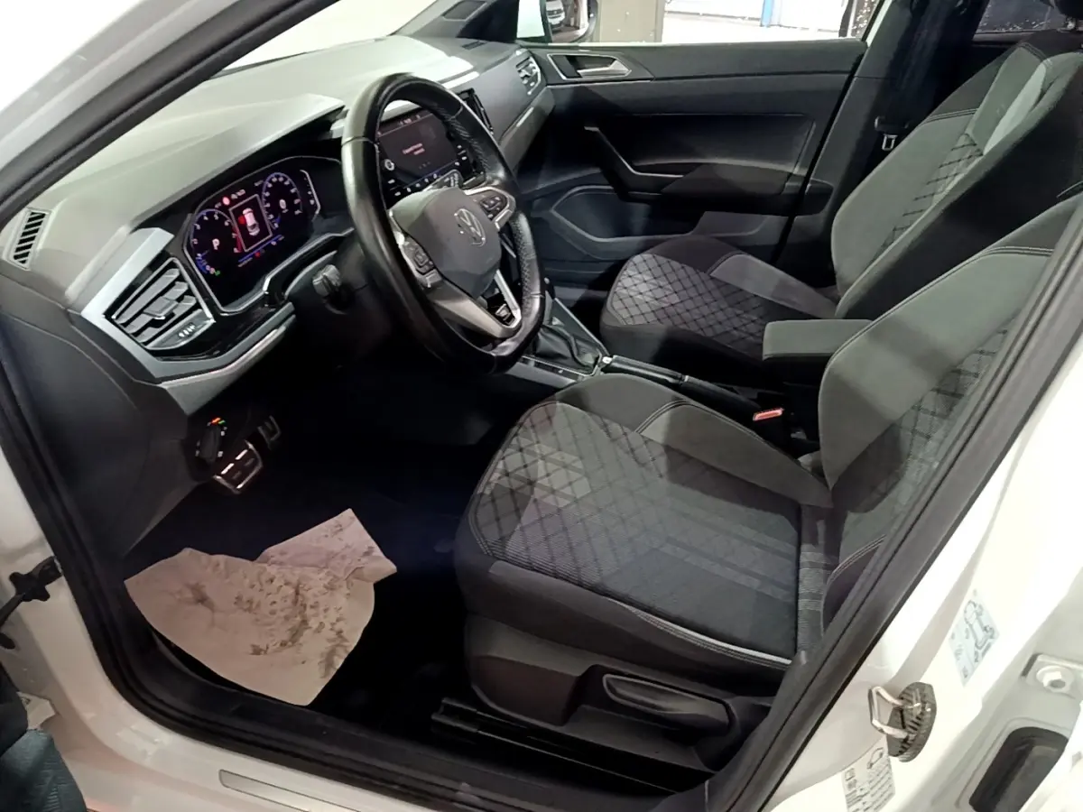 Vue intérieure côté conducteur d'un Volkswagen Taigo blanc 2022, volant cuir alu multifonctions et sièges tissu gris à motifs.