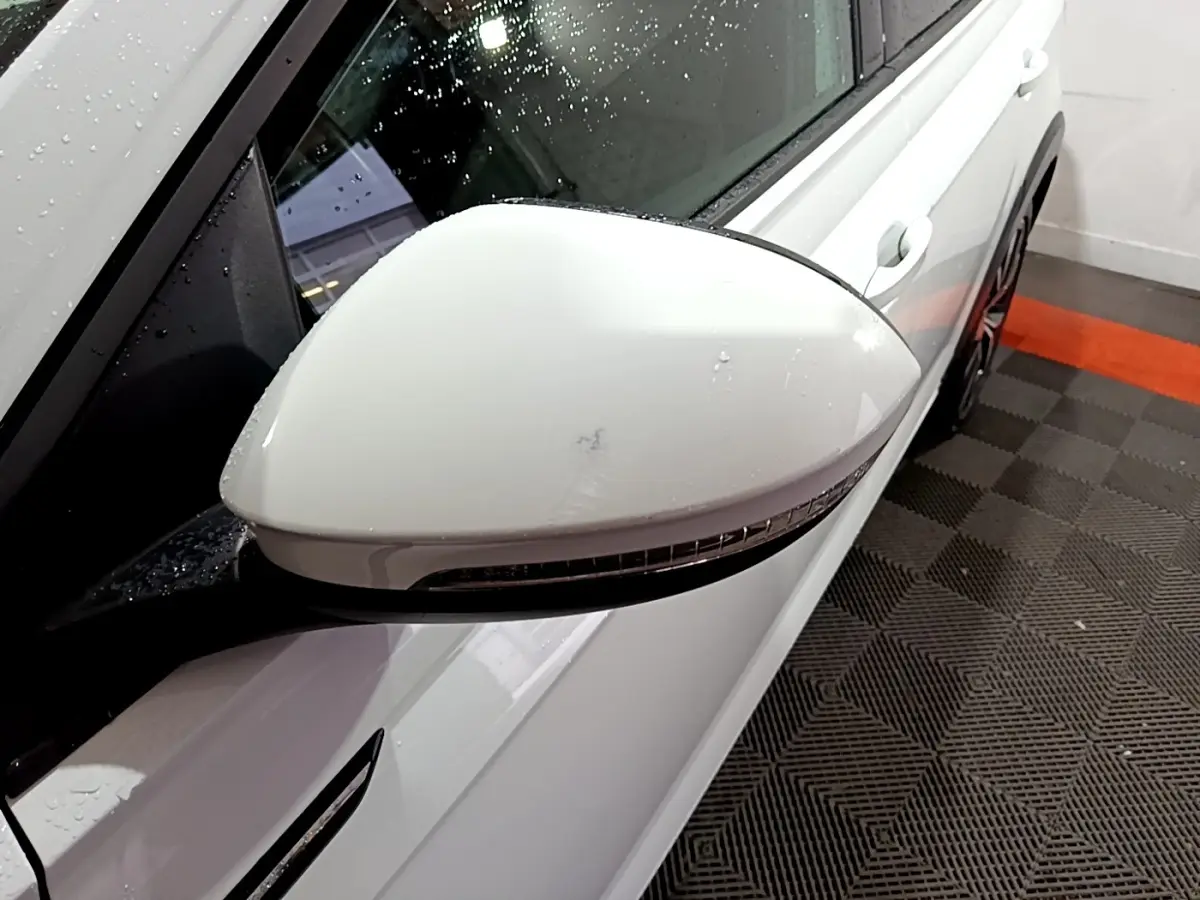 Gros plan sur le rétroviseur droit blanc du Volkswagen Taigo 1.0 TSI 110 DSG R-Line, avec carrosserie blanche visible.