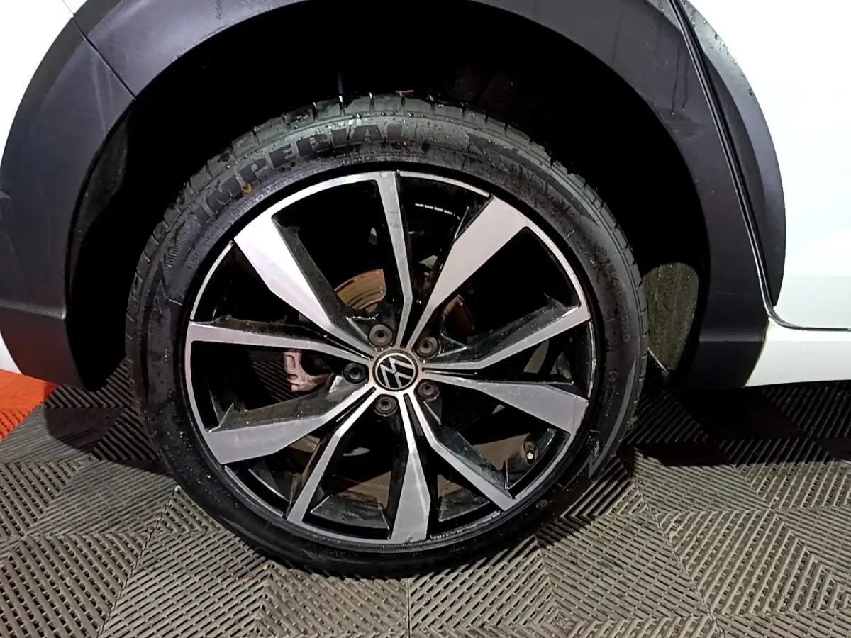 Gros plan sur la roue avant droite d’un Volkswagen Taigo blanc, jante alliage noir et argentée R-Line.