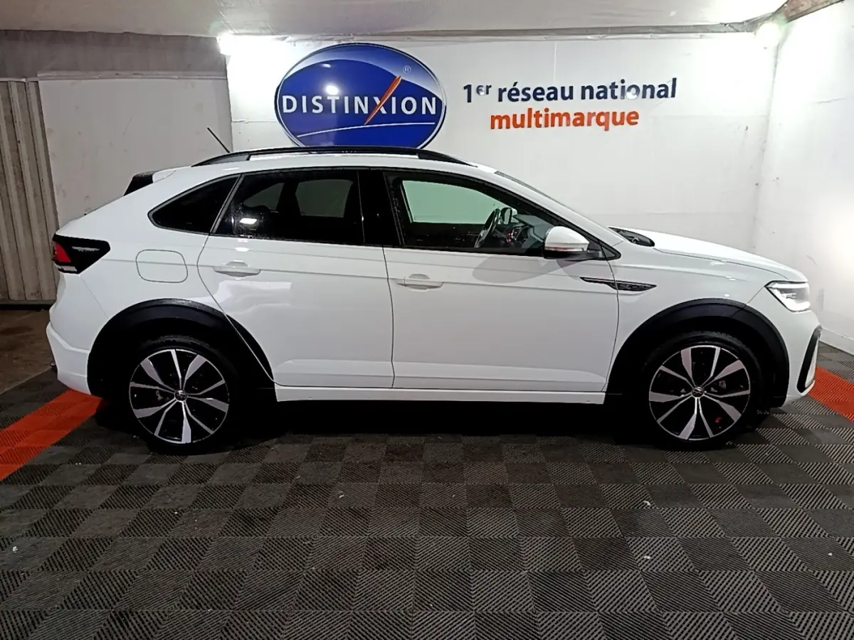 Vue de profil côté gauche d'un Volkswagen Taigo blanc 2022 R-Line avec jantes noires et toit noir dans un garage.