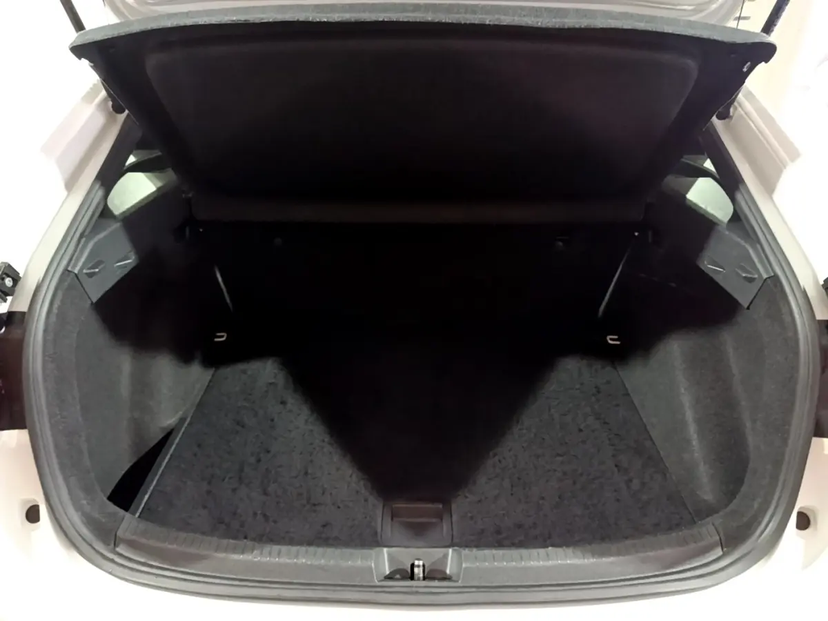 Vue du coffre ouvert d'une Volkswagen Taigo blanc, montrant l'espace de rangement intérieur vide et la tablette arrière relevée.