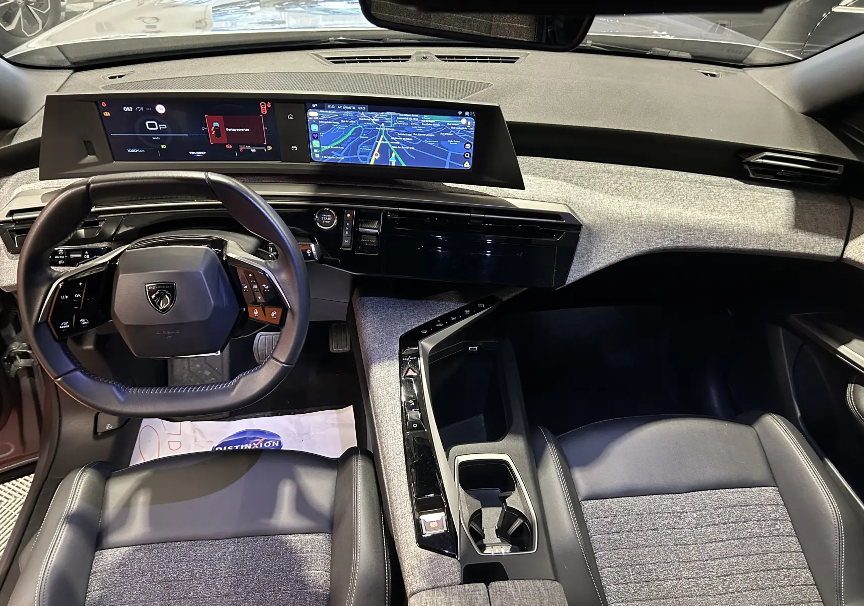 Vue intérieure du poste de conduite du Peugeot 5008 hybride 2025, avec volant compact et double écran numérique.