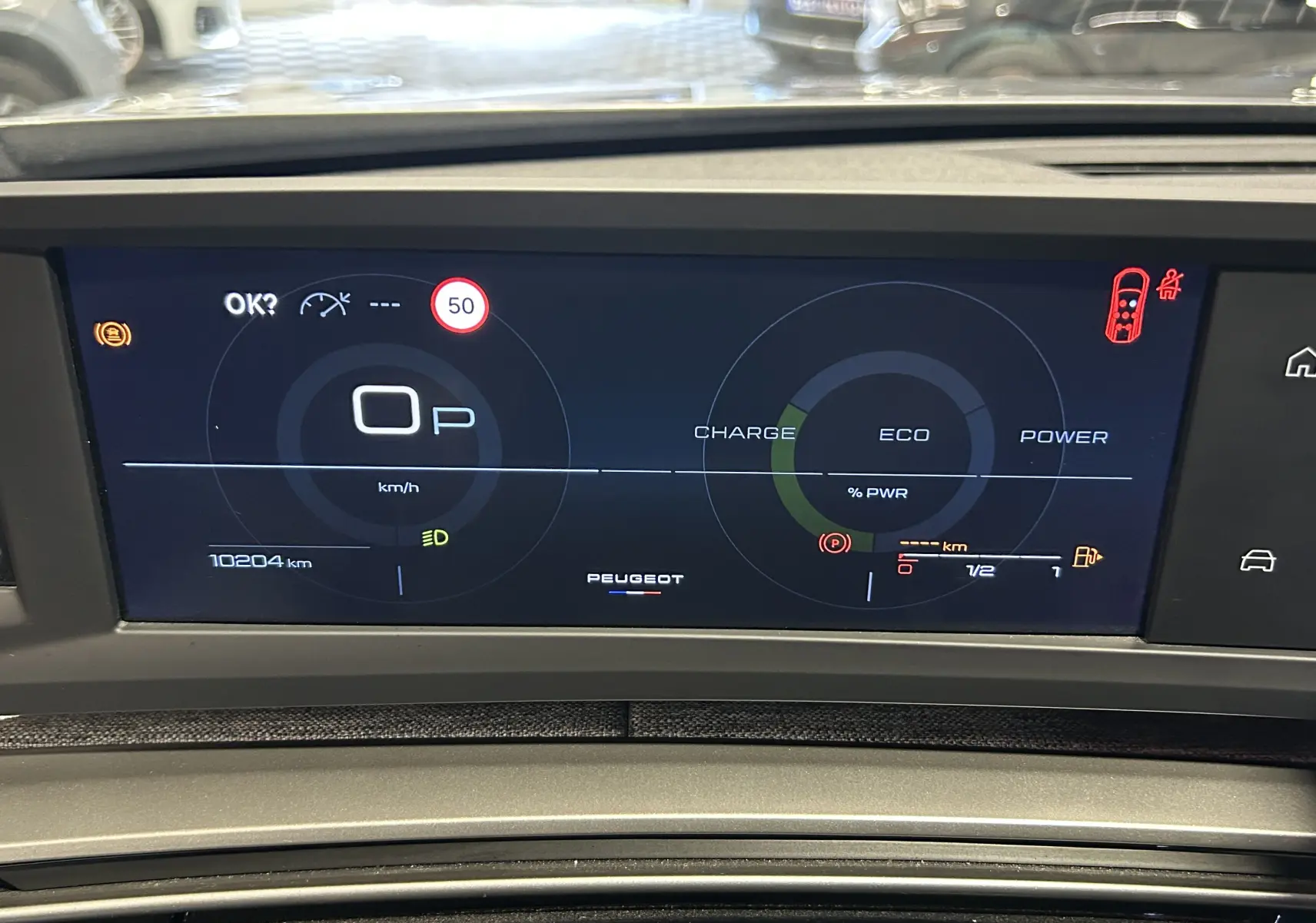 Tableau de bord numérique du Peugeot 5008 gris Artense, affichage vitesse, charge hybride et alertes visibles.