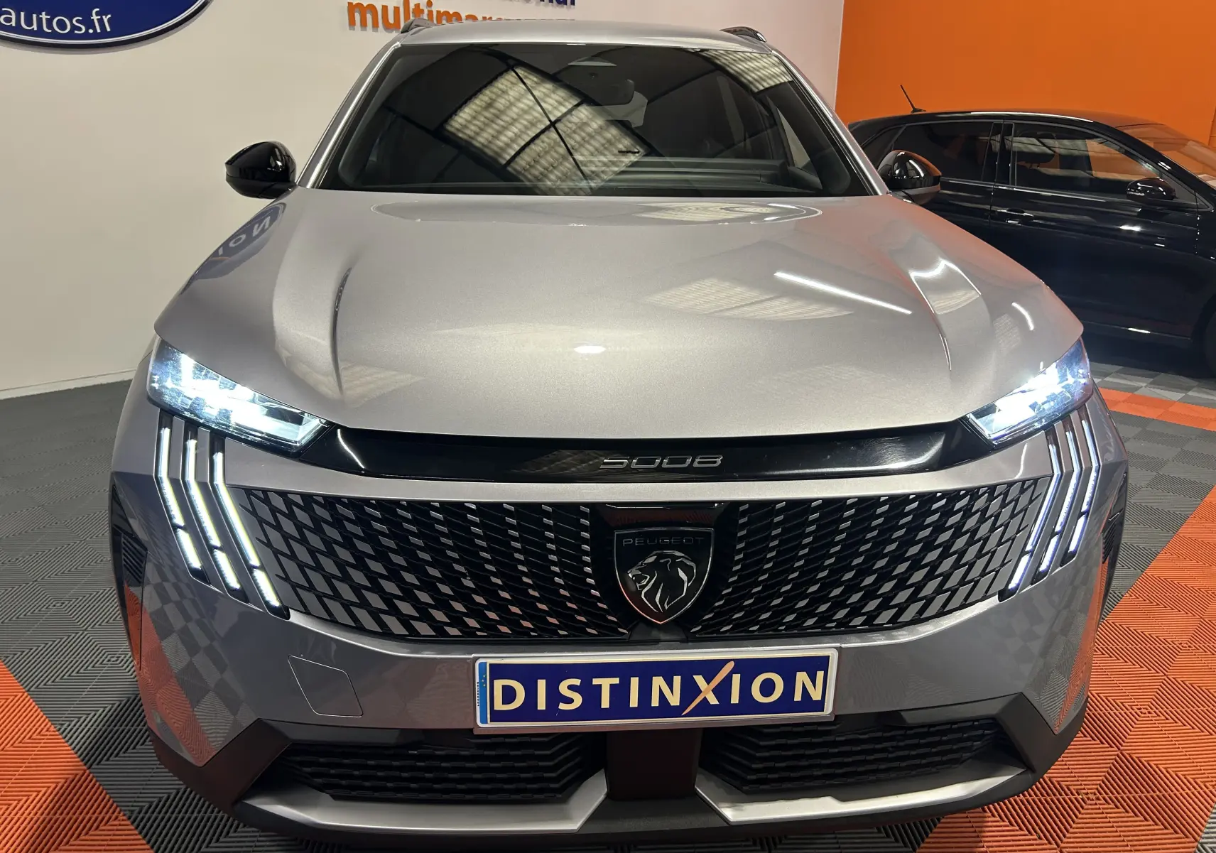 Vue avant du Peugeot 5008 gris Artense avec calandre noire et feux LED allumés en intérieur showroom.