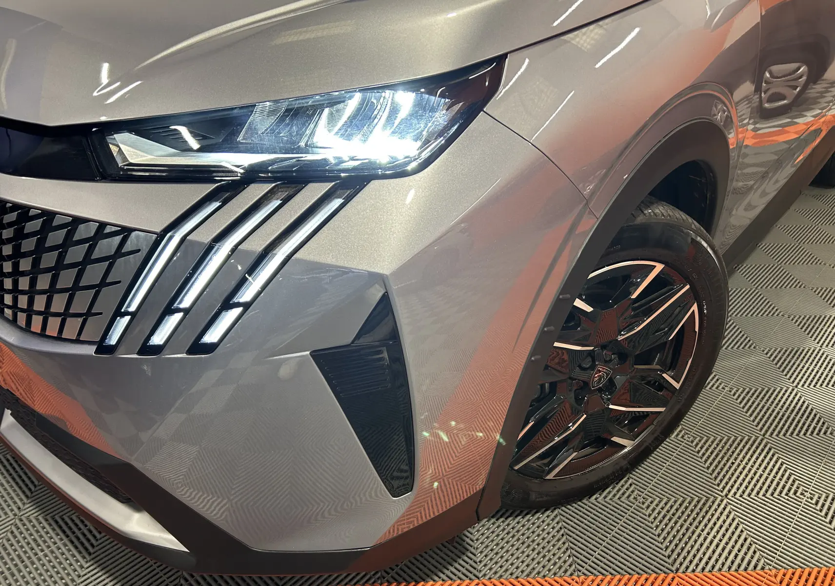 Gros plan sur l'avant droit gris Artense du Peugeot 5008 III Hybrid, mettant en valeur le phare LED et la jante noire.