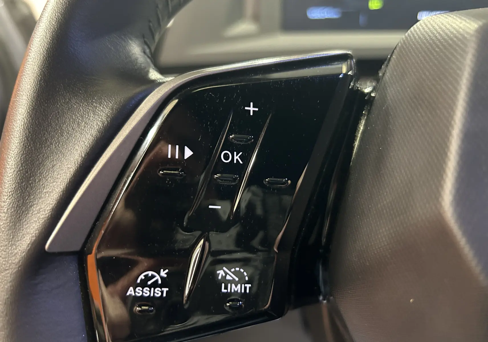 Gros plan sur les commandes noires du volant côté gauche du Peugeot 5008 hybride gris Artense, avec boutons de réglage et assistance.