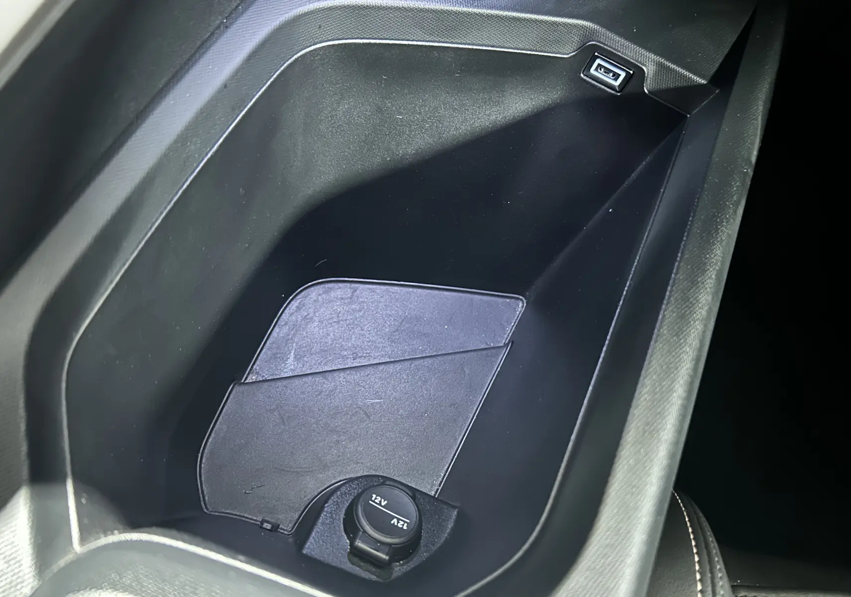 Gros plan sur la console centrale intérieure noire du Peugeot 5008 avec prise USB et prise 12V visible.