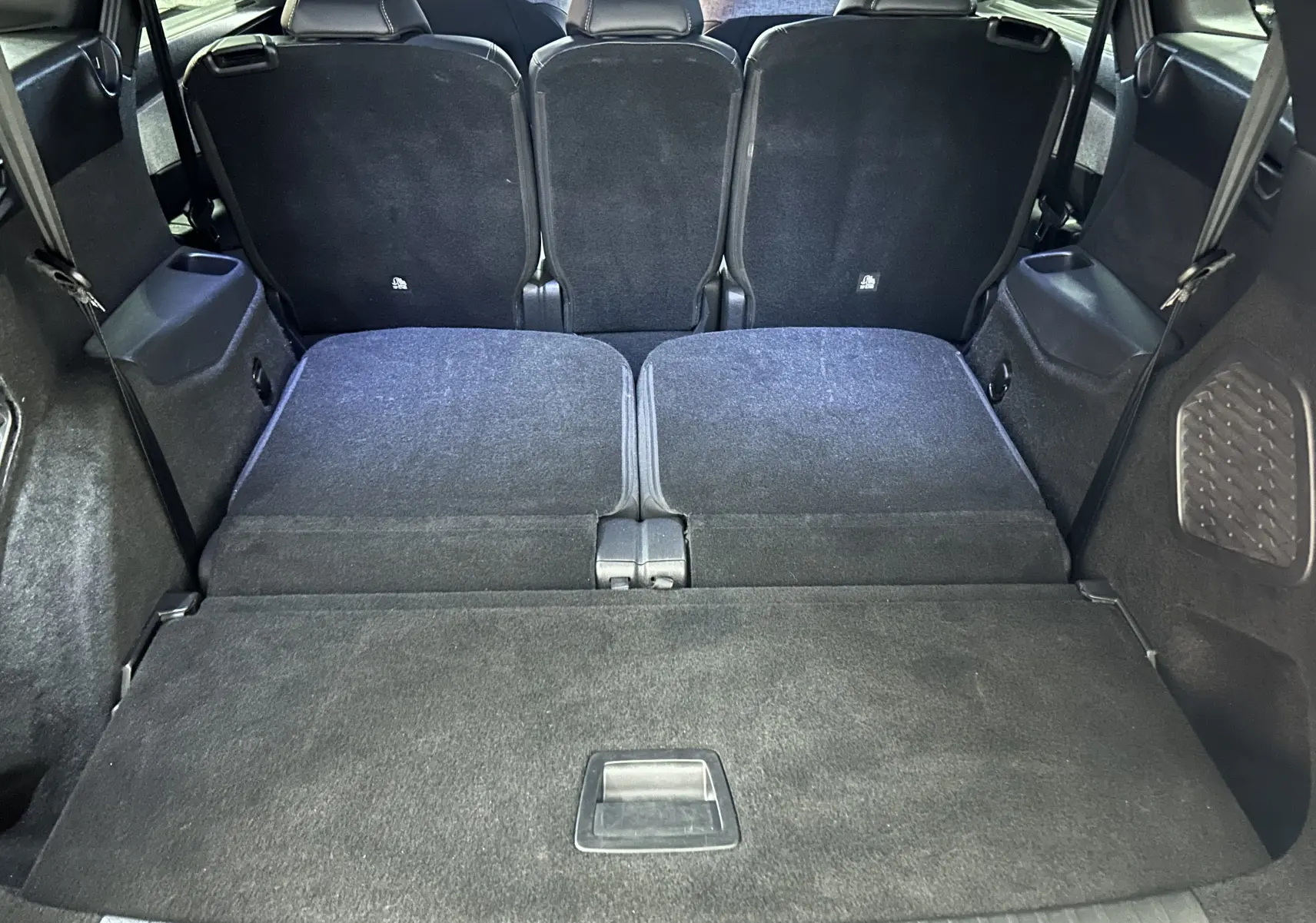 Vue du coffre arrière du Peugeot 5008 hybride 2025 avec sièges rabattus et revêtement intérieur noir.