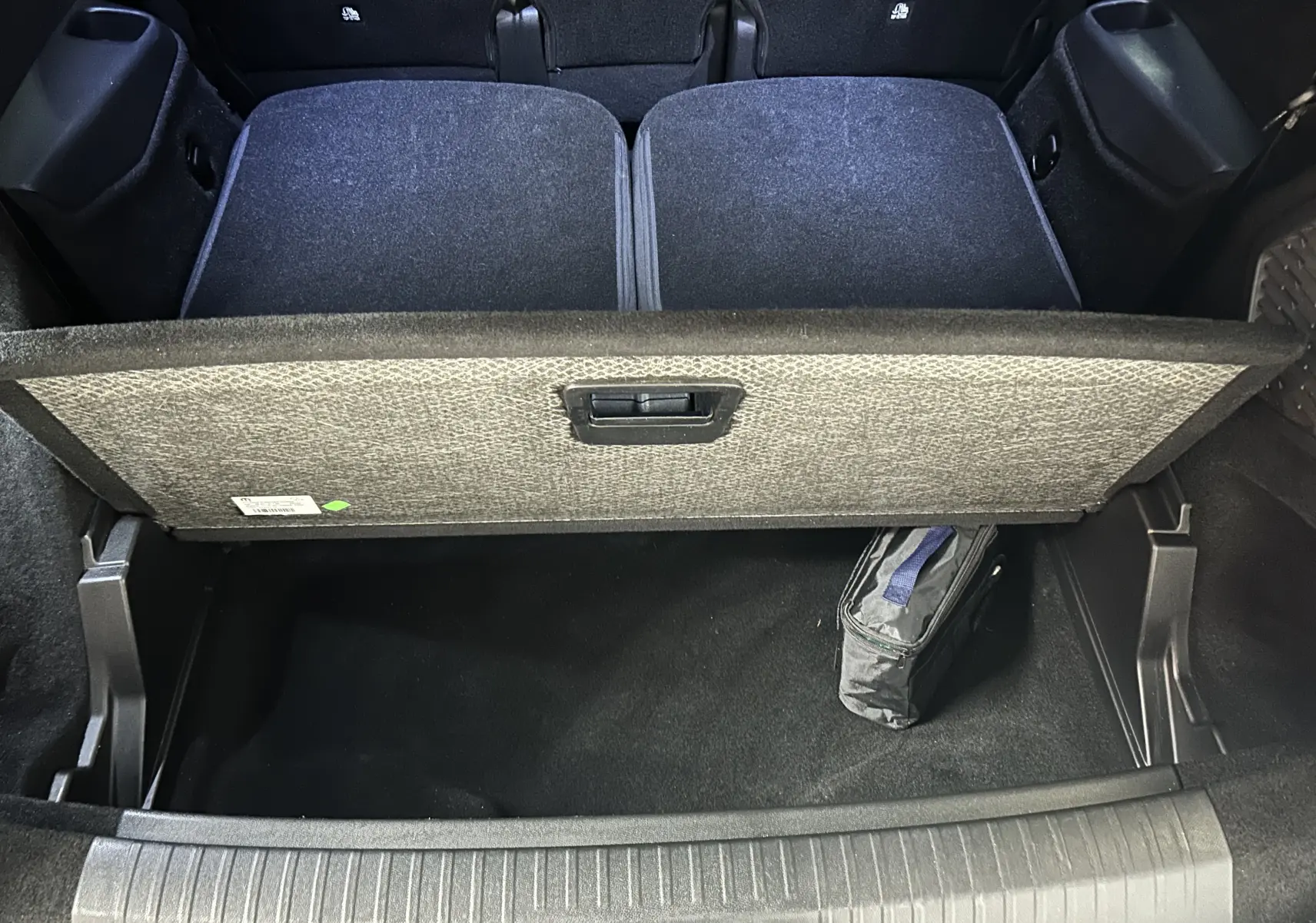 Vue plongeante sur le coffre ouvert du Peugeot 5008 gris Artense, montrant la tablette de séparation et un sac de rangement noir.