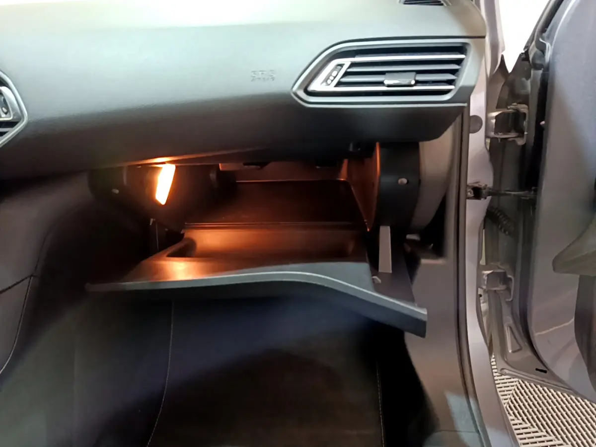 Gros plan sur la boîte à gants ouverte côté passager d'une Peugeot 308 gris clair, éclairée intérieurement.
